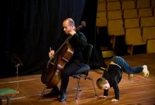 Un niño baila junto a un violoncellista